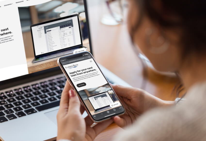 Woman holding a phone with Luzerne Bank website on both her phone and laptop in background.