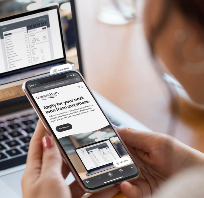 Woman holding phone that displays the Luzerne Bank website while in the background the digital banking appears on a laptop.